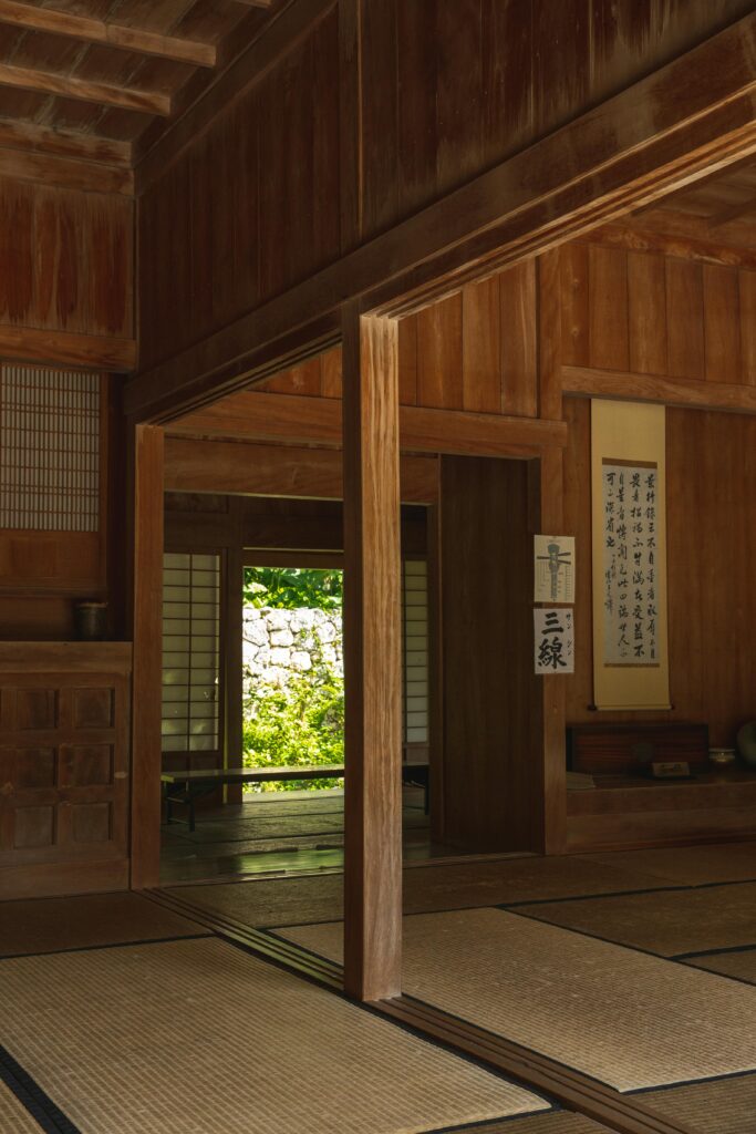 A serene Japanese minimalist room with wooden walls, tatami flooring, and a view of a garden through an open doorway.